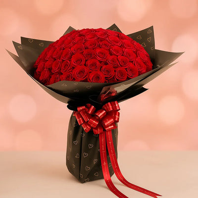 Bouquet of red roses wrapped in black paper with a red ribbon on a pink background