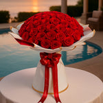 Load image into Gallery viewer, Bouquet of red roses on a white stand with a red ribbon by a poolside.
