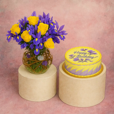 Yellow and purple flowers in a vase next to a yellow cake with 'Happy Birthday' text on a pink background