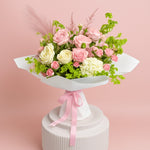 Load image into Gallery viewer, Bouquet of pink and white roses with greenery on a white pedestal against a pink background
