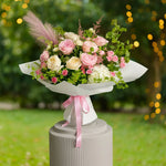 Load image into Gallery viewer, Bouquet of pink and white flowers with greenery on a pedestal against a blurred outdoor background.
