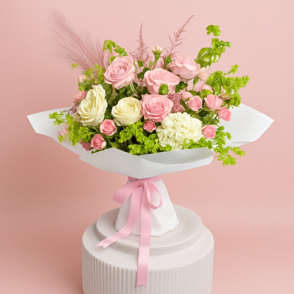 Bouquet of pink and white roses with greenery on a white pedestal against a pink background
