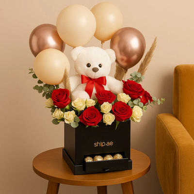Decorative arrangement with a teddy bear, balloons, and flowers on a table.