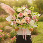 Load image into Gallery viewer, Person holding a bouquet of pink, white, and green flowers with pink feathers in a garden setting.
