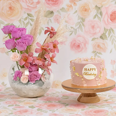 Pink birthday cake with 'Happy Birthday' text and a vase of pink flowers on a floral background