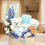 Load image into Gallery viewer, Gift basket with a teddy bear, flowers, and baby items in a living room setting.
