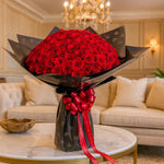 Load image into Gallery viewer, Bouquet of red roses with a black wrap and red ribbon on a marble table in a luxurious room.

