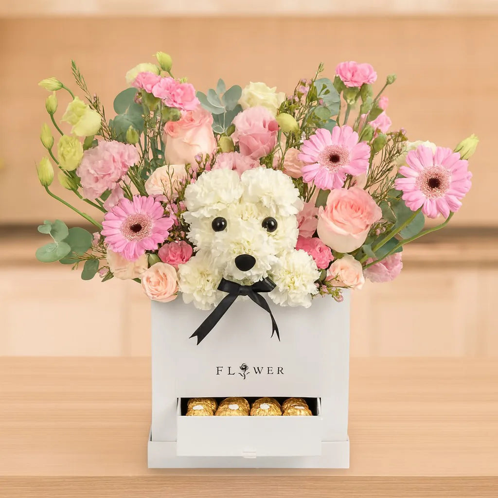 Floral arrangement with a white dog-shaped toy and pink flowers in a box, set against a wooden background.