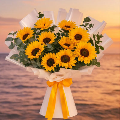 Bouquet of sunflowers with a yellow ribbon against a sunset ocean backdrop
