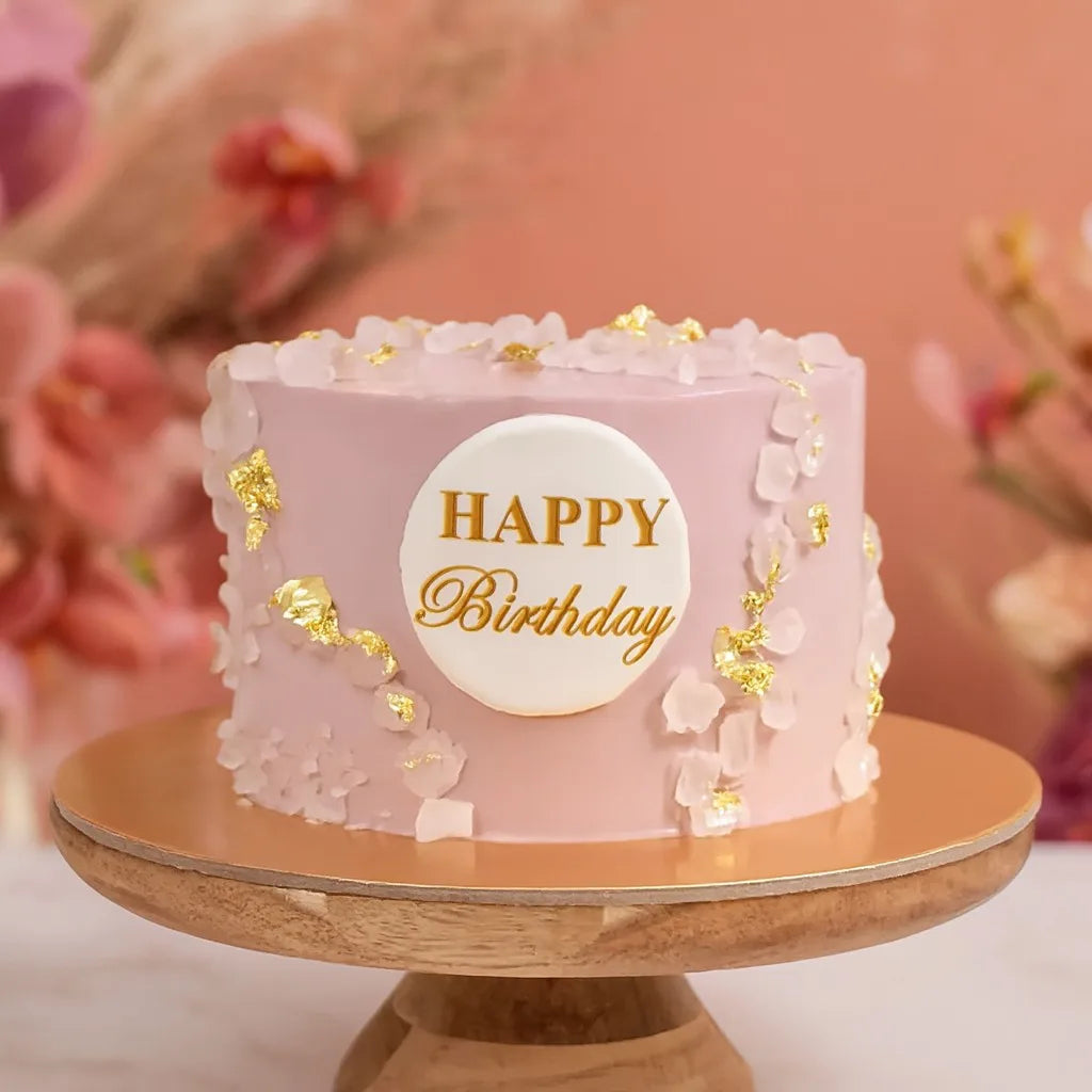 Pink birthday cake with 'Happy Birthday' text on a wooden stand against a blurred floral background