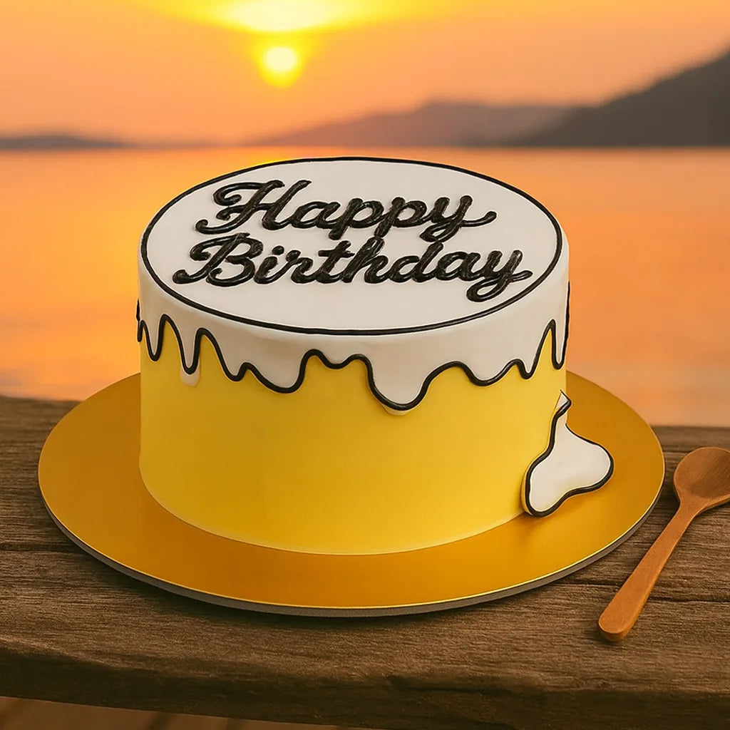 Yellow birthday cake with 'Happy Birthday' on a wooden table against a sunset backdrop