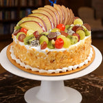 Load image into Gallery viewer, Fruit cake with apples, grapes, and kiwis on a white cake stand.
