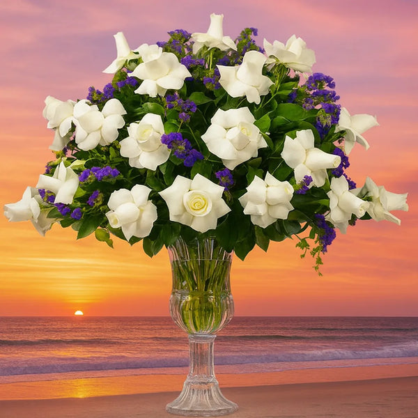 Bouquet of white flowers in a glass vase against a sunset beach backdrop
