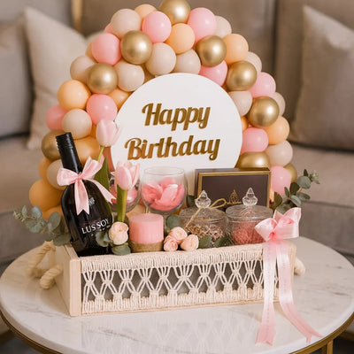 Birthday gift basket with balloons, wine, and decorative items on a table.