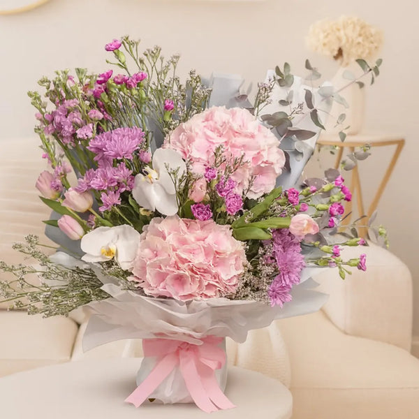 Bouquet of pink and purple flowers with greenery on a light background