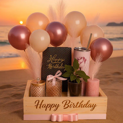 Birthday arrangement with balloons, candles, and plants on a beach at sunset.
